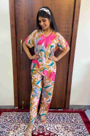 Woman wearing a colorful floral cotton co-ord set featuring pink, mustard, and blue abstract prints, standing indoors on a red and navy patterned rug