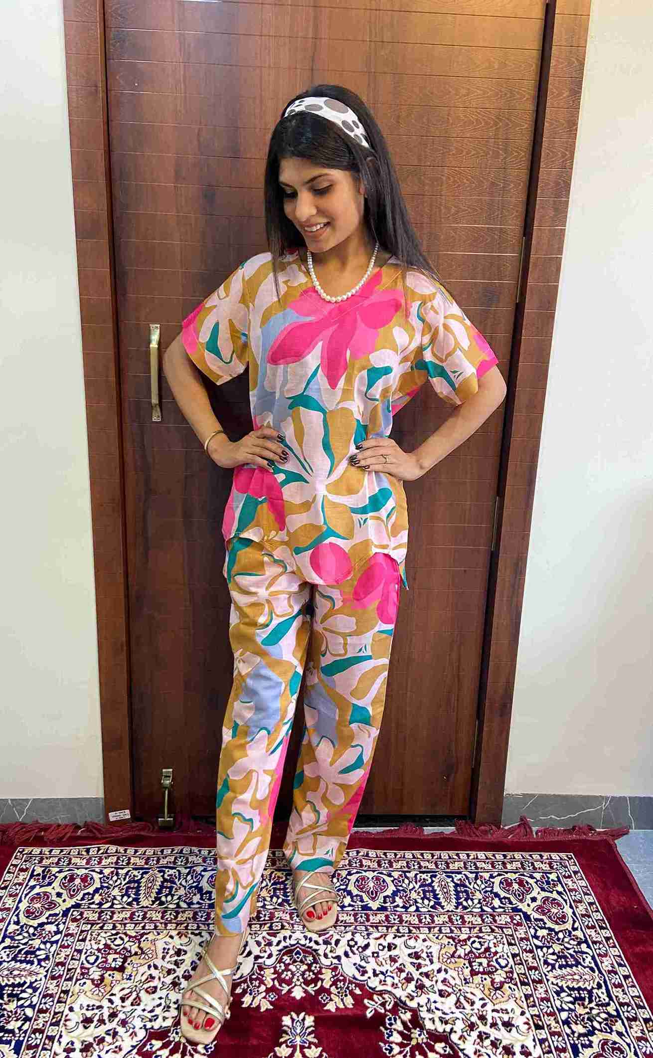 Woman wearing a colorful floral cotton co-ord set featuring pink, mustard, and blue abstract prints, standing indoors on a red and navy patterned rug