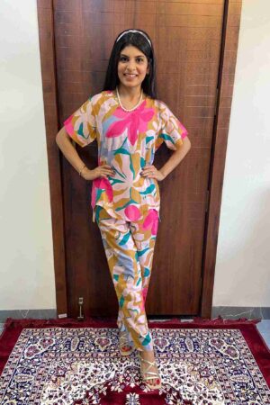 Woman wearing a colorful floral cotton co-ord set featuring pink, mustard, and blue abstract prints, standing indoors on a red and navy patterned rug